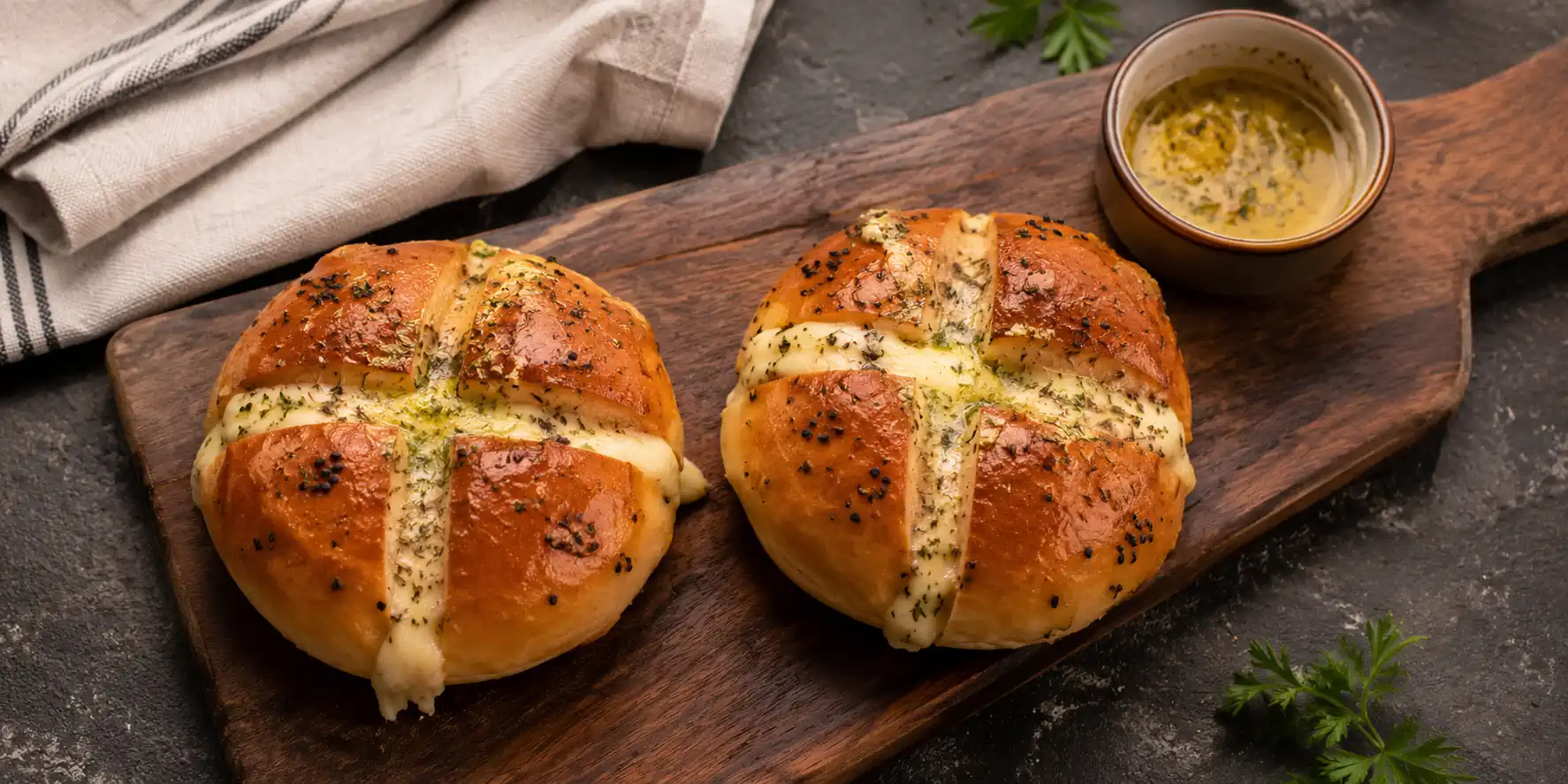 A wooden board with two golden-brown Korean cream cheese garlic bread rolls cut open, showing creamy white cheese filling, garlic butter glaze, and parsley flakes on top.